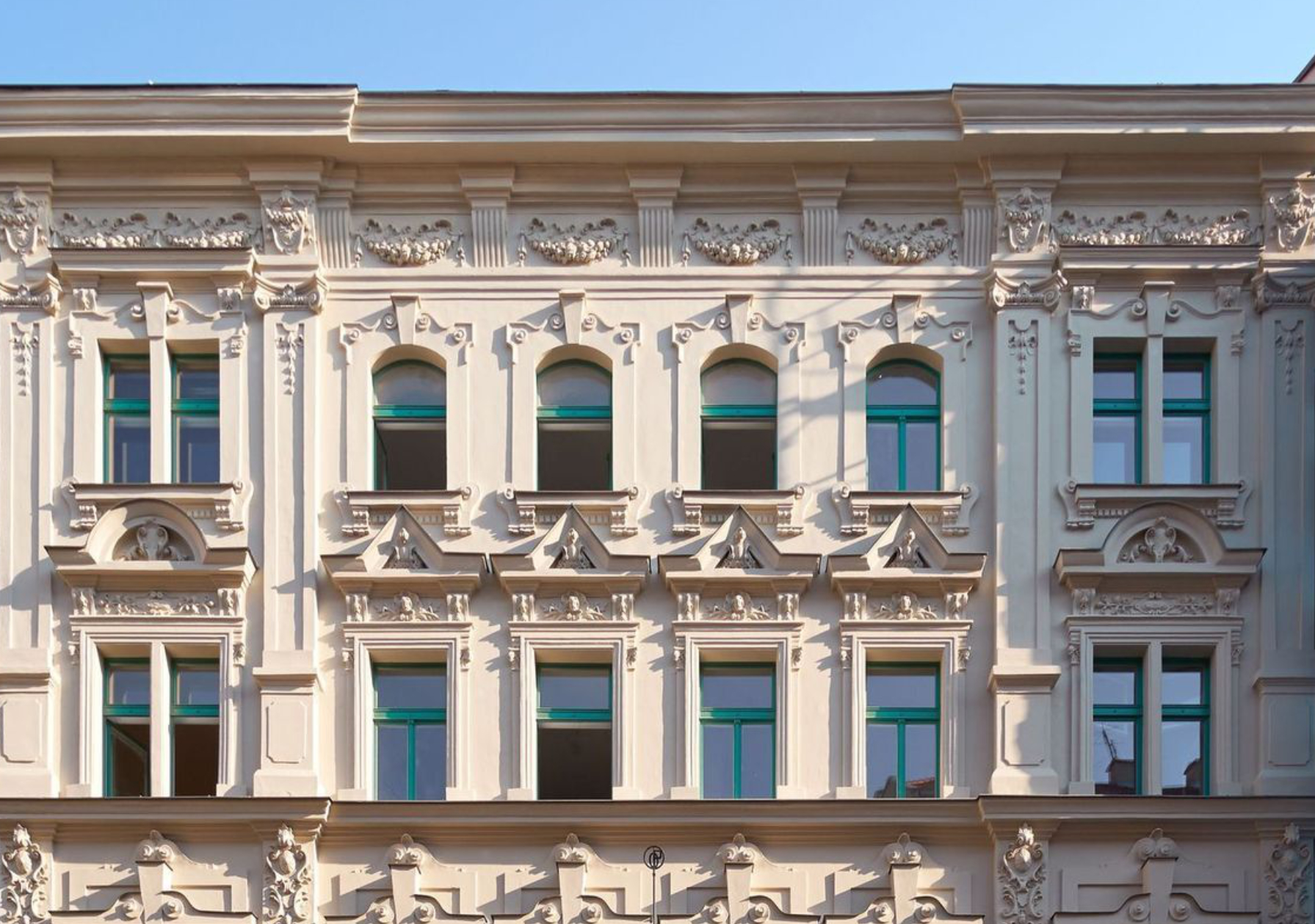 Ornate historic building facade with decorative stucco, arched and rectangular windows framed in green, showcasing intricate relief details.