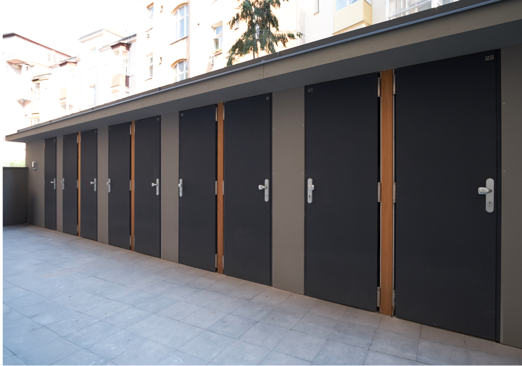 Row of dark storage lockers with metal handles along a concrete courtyard.