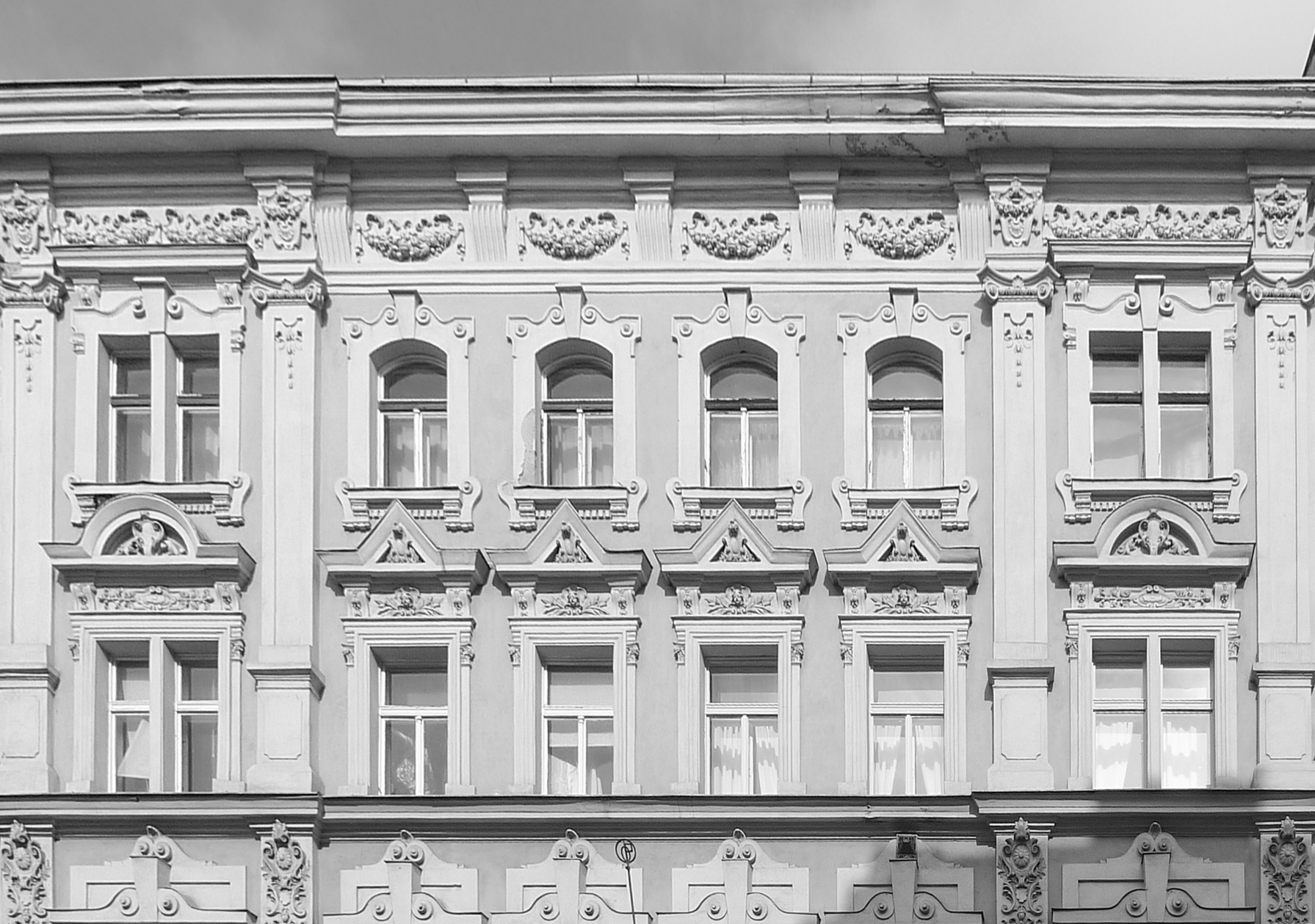 Historic building facade with ornate decorative molding, tall arched and rectangular windows in a symmetrical row.